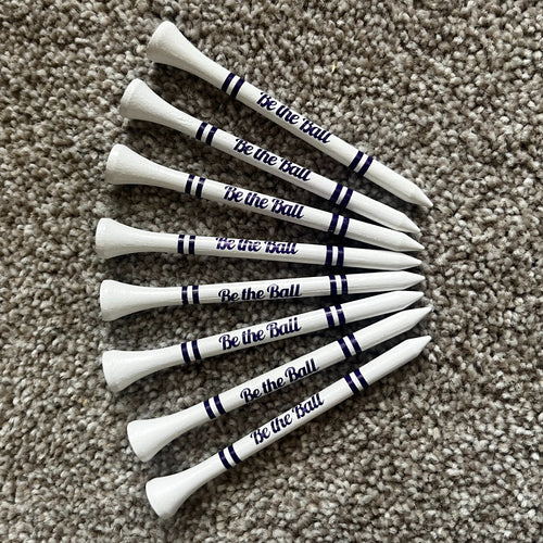 White golf tees with 'Be the Ball' text on a beige carpet